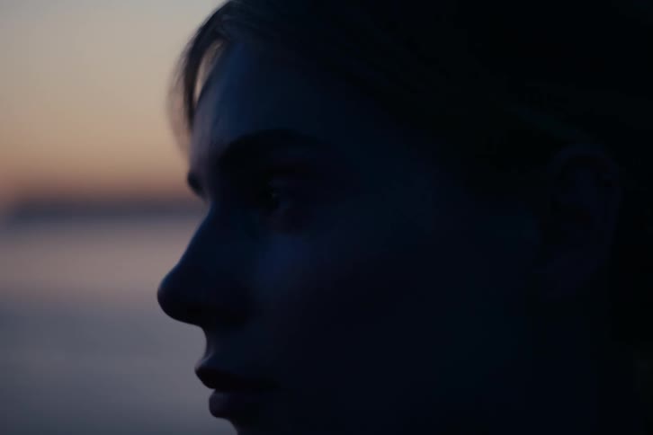 Extreme close-up profile of a pensive young woman's face as she gazes at the ocean during twilight