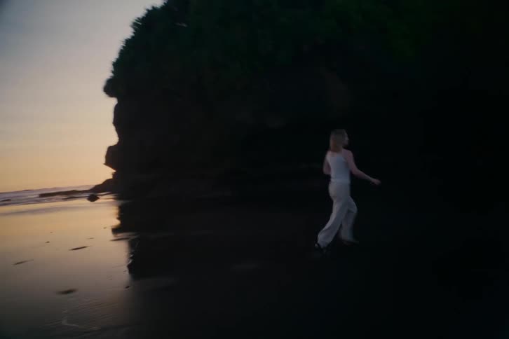 Dreamy handheld footage follows a joyful woman running on a secluded beach at dusk