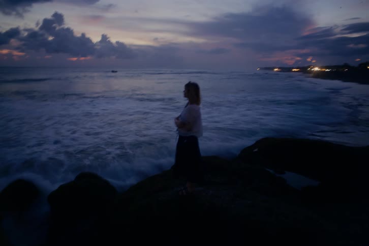 An artistic long exposure shot of a pensive woman silhouetted against the ocean at dusk