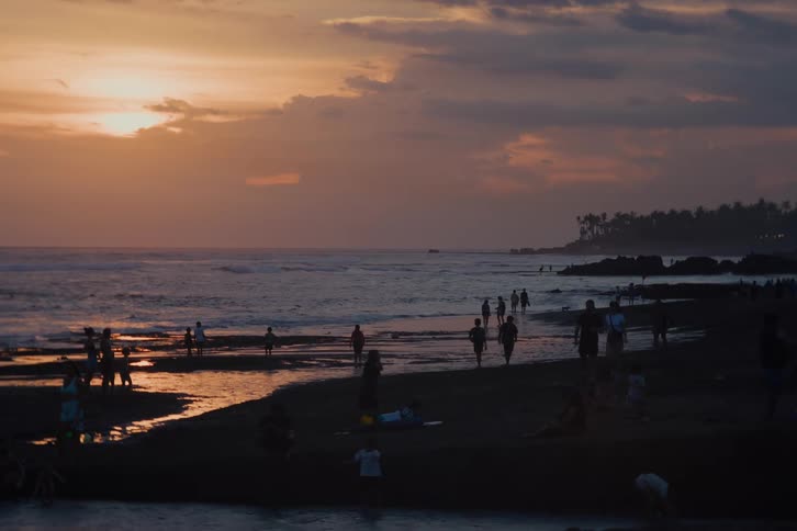 Silhouettes of a crowd of people relax and play on a tropical beach during a beautiful and serene sunset over the ocean