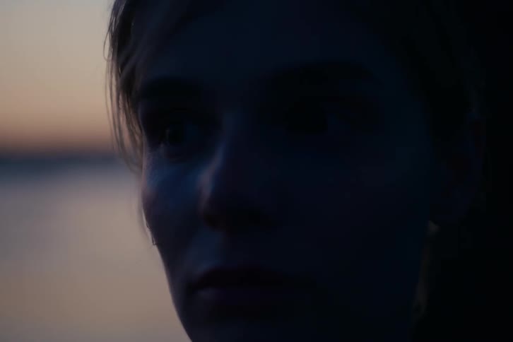A dramatic close-up of a woman's face in shadow with a tear rolling down her cheek at sunset