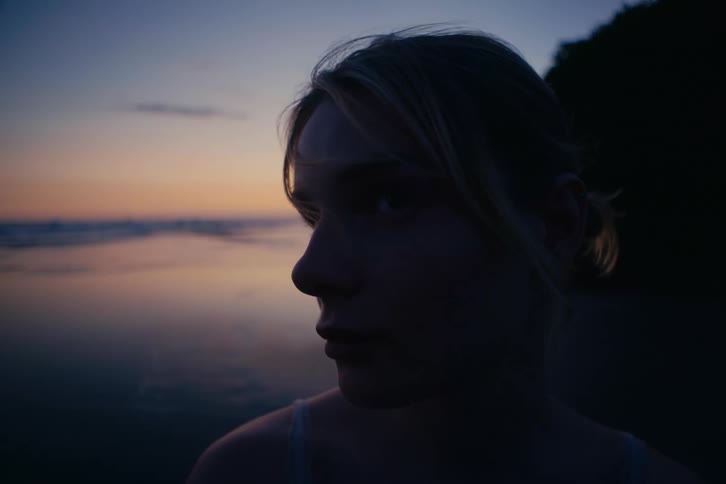Close-up profile of a young woman's face silhouetted against the ocean at sunset