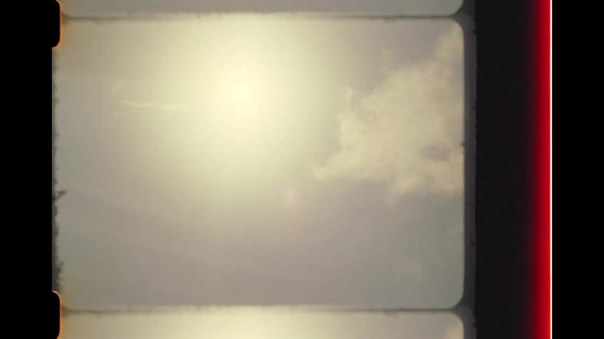 A vintage 8mm film clip pans up from a lush green hill to the bright sun in a cloudy sky, complete with authentic light leaks and film grain