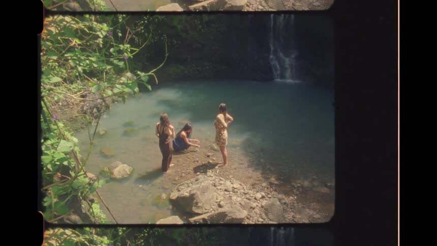Vintage film captures three women enjoying a serene jungle pool at the base of a waterfall
