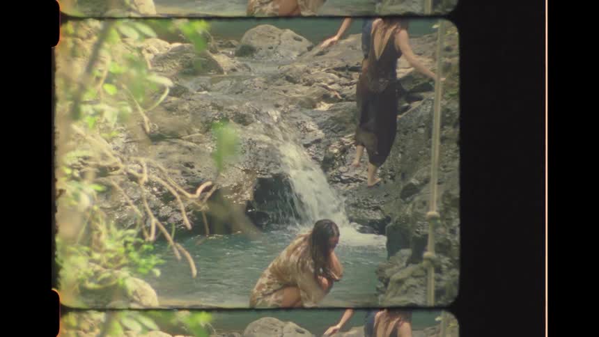Women in dresses wade and climb rocks by a jungle waterfall in this vintage-style film