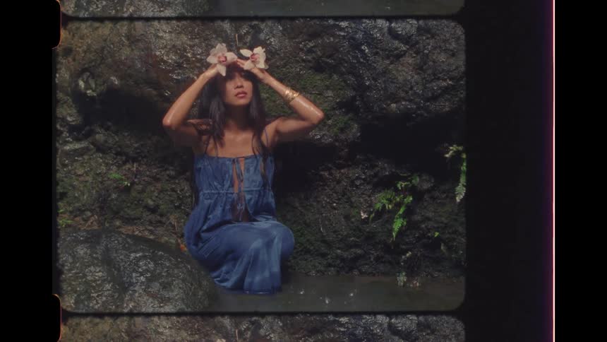Vintage film-style cinemagraph of a serene woman with a flower crown sitting in a jungle waterfall pool