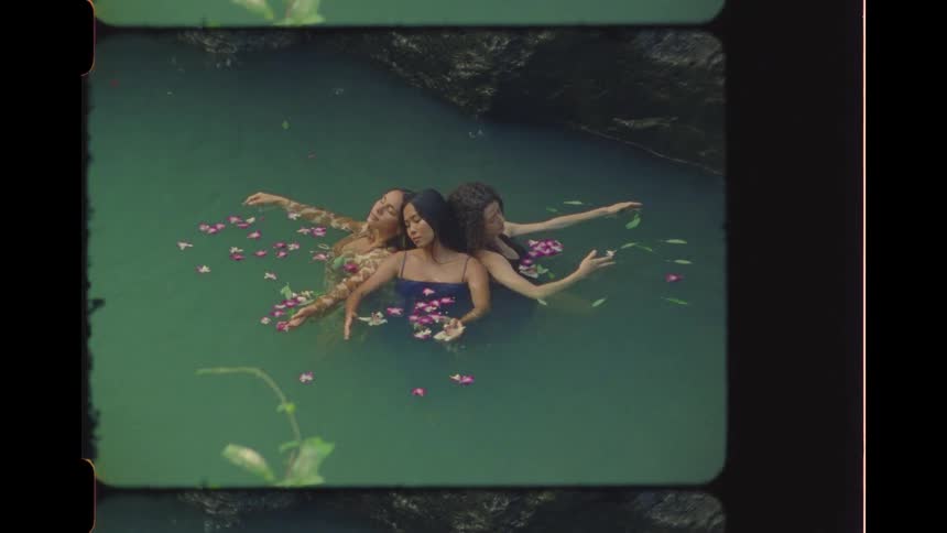 High angle vintage-style shot of three beautiful women peacefully floating in tranquil green water with flower petals