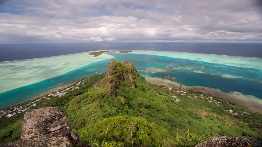 Breathtaking time-lapse from a mountain peak reveals a lush tropical island, vibrant turquoise lagoon, and a hiker admiring the scenic view