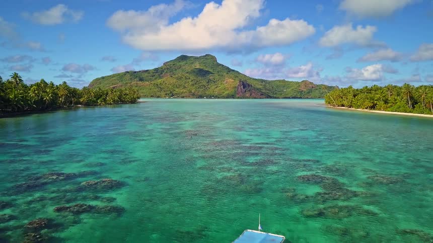 Stunning aerial view of a boat anchored in a turquoise lagoon with a lush tropical mountain island in the background