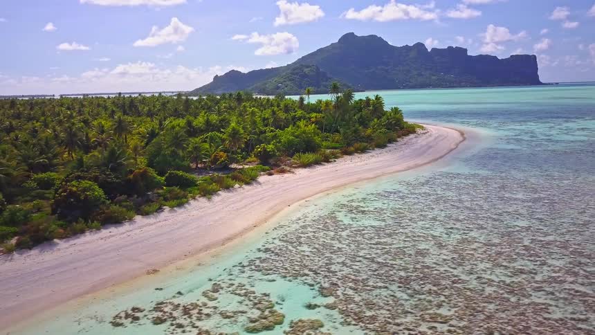 An aerial view reveals a stunning tropical island with a white sand beach, a turquoise lagoon, and a vibrant coral reef