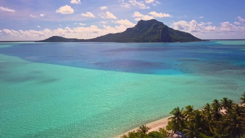 An idyllic aerial view slowly pulls back over a vibrant turquoise lagoon to reveal the shoreline of a tropical paradise island