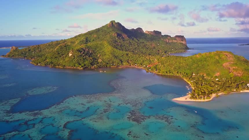 A beautiful aerial view of a remote tropical island with a lush green mountain surrounded by a turquoise lagoon and coral reef