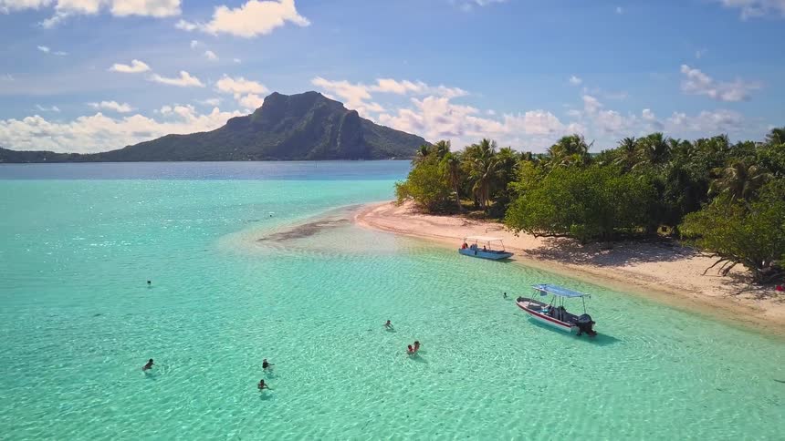 A stunning aerial view captures people swimming in a crystal-clear turquoise lagoon surrounding a tropical island paradise in Bora Bora