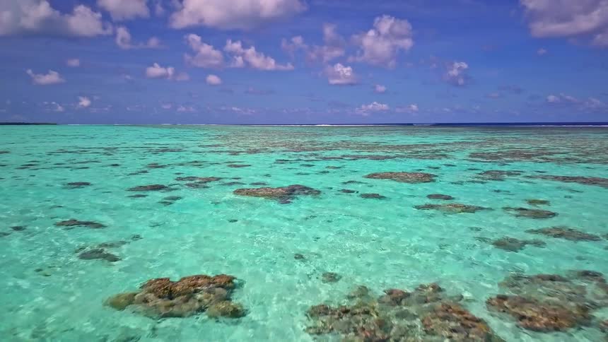 Breathtaking aerial journey over a shallow coral reef in a tranquil turquoise sea under a cloudy blue sky