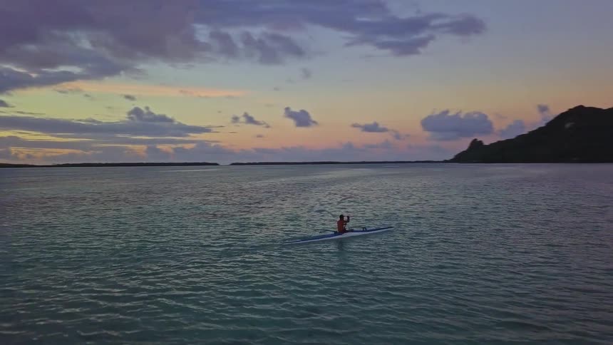 A lone person paddles an outrigger canoe across the calm, tropical ocean during a beautiful and colorful sunset