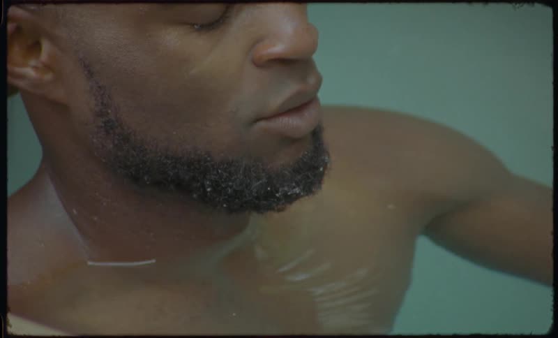A serene man with his eyes closed finds tranquility while soaking in a milky bath in this vintage-style footage