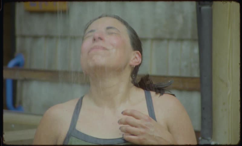 Slow motion vintage-style footage of a happy woman washing her face and relaxing under an outdoor shower