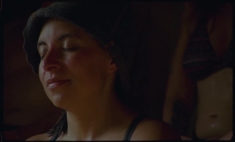 A serene woman with a relaxed expression enjoys the warm, calming atmosphere of a dimly lit sauna