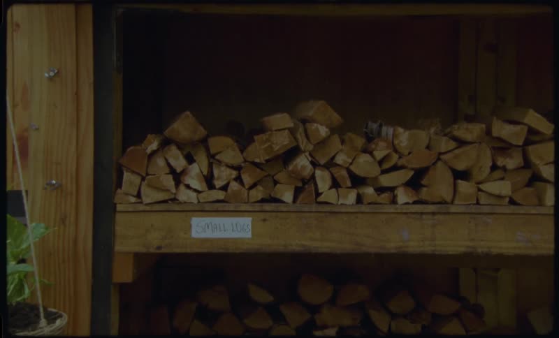 A person selects and takes small logs of firewood from a rustic wooden storage shelf