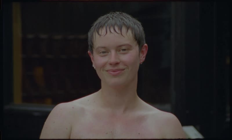 An intimate, filmic portrait of an androgynous person with wet hair looking directly into the camera and breaking into a genuine smile