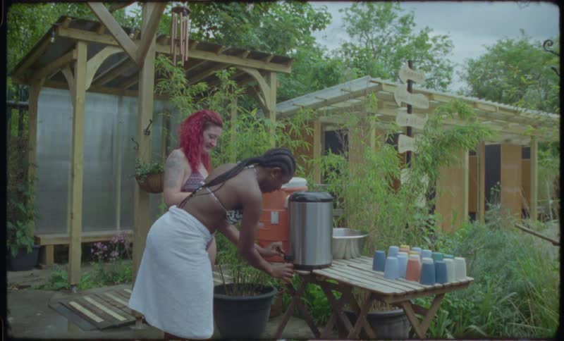 Two women in bikinis enjoy drinks and conversation in a lush, green garden retreat