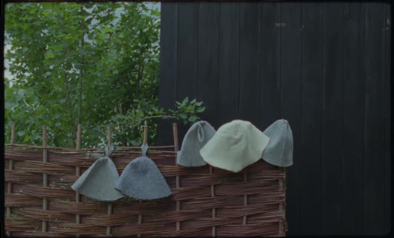 A collection of felt sauna hats drying on a rustic wicker fence