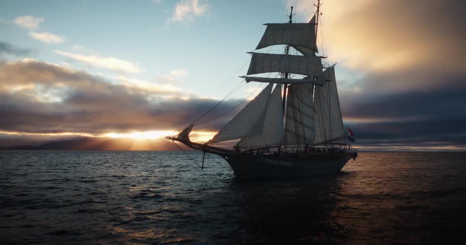 A majestic tall ship with full sails cruises across the open ocean during a dramatic and beautiful sunset