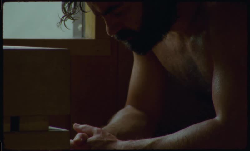 A bearded man meditates with his eyes closed, sweating inside a traditional wooden sauna