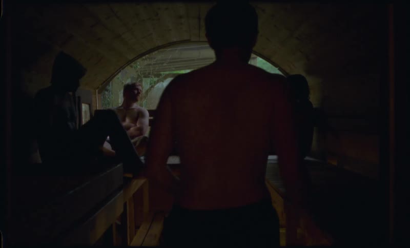 Men gather to relax and socialize inside a traditional wooden barrel sauna with a vintage film aesthetic