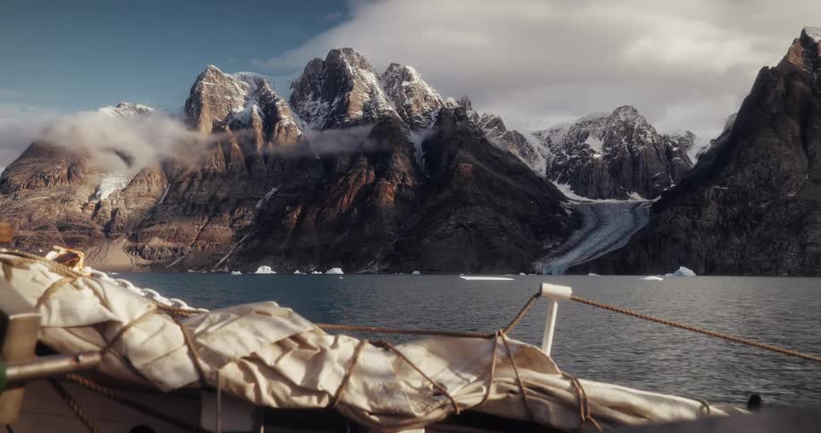 Epic view from a boat of a dramatic, snow-capped mountain range and a glacier in an arctic fjord