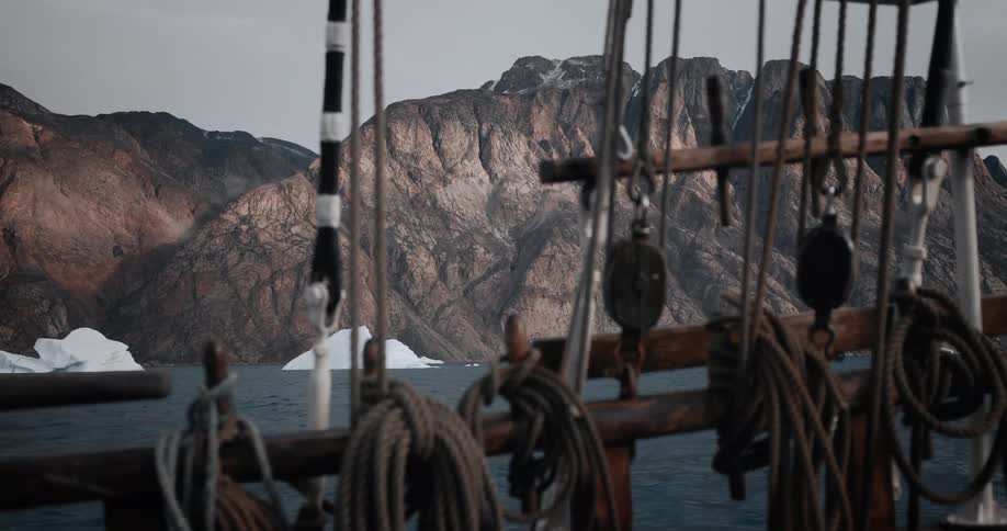 Slow rack focus from the weathered ropes and rigging of an old ship to the majestic arctic mountains and icebergs in the distance