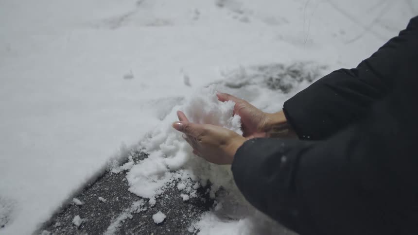 A close-up of a person's hands slowly scooping up a handful of fresh white snow in the winter