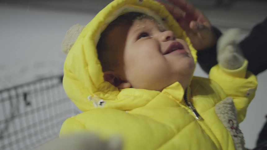 An adorable baby in a bright yellow snowsuit laughs with pure delight, catching snowflakes on its tongue during its first snowfall at night