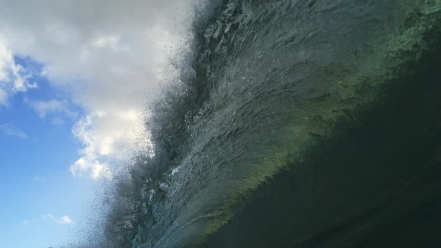 A stunning slow-motion, in-water perspective of a powerful ocean wave cresting and breaking under a cloudy sky