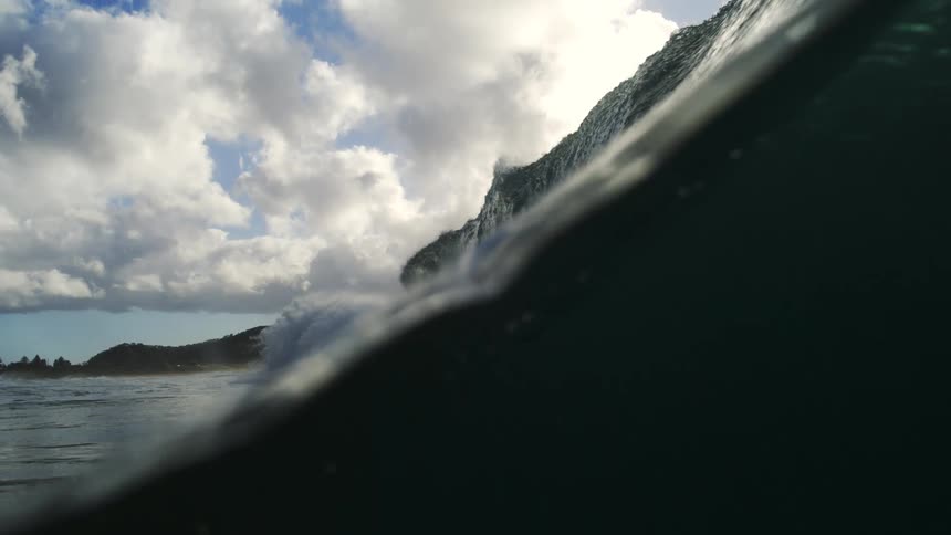 An epic ocean wave filmed in super slow motion rises and crests before the camera sinks below the surface into the deep