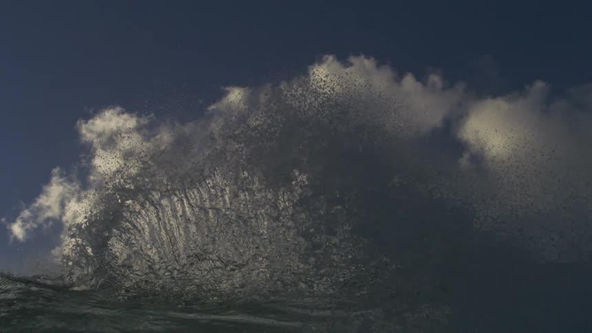 An epic, slow-motion close-up of a powerful ocean wave cresting against a beautiful blue sky