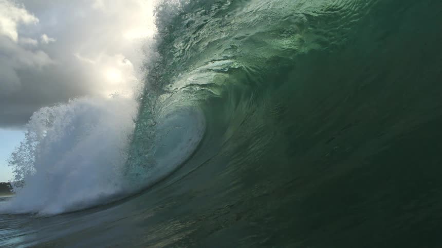 An epic slow-motion shot from inside the barrel of a massive green ocean wave as it curls over the camera