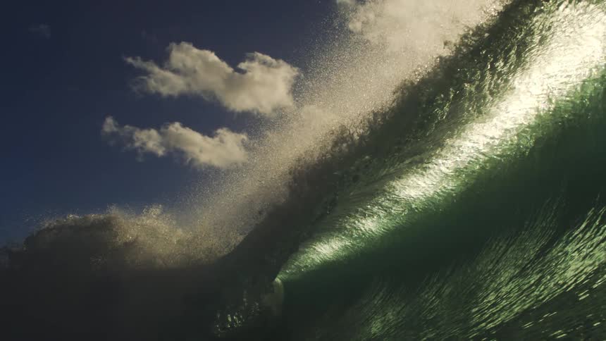 A stunning slow-motion view from inside a barreling ocean wave as sunlight illuminates the turquoise water against a blue sky