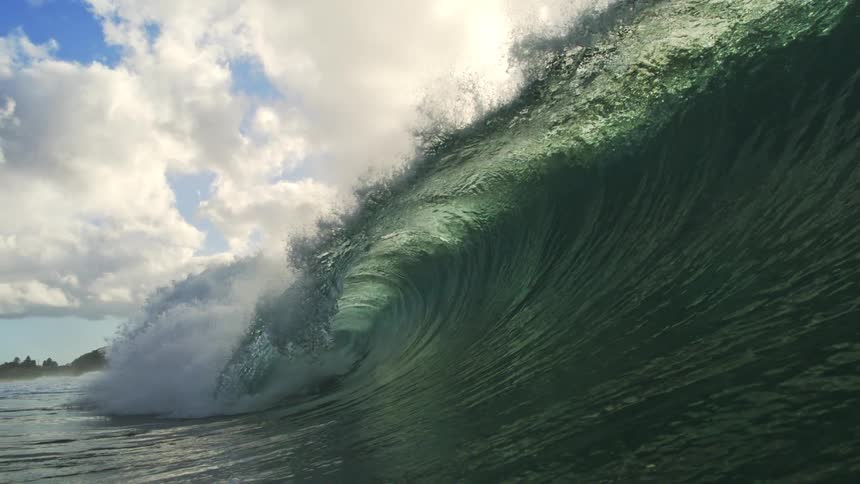 Sunlight illuminates a majestic dark green ocean wave as it curls into a perfect barrel in stunning super slow motion