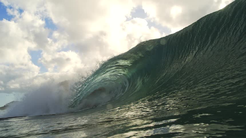 A majestic ocean wave forms a perfect barrel in cinematic slow motion, with the sun and clouds visible through the curling water