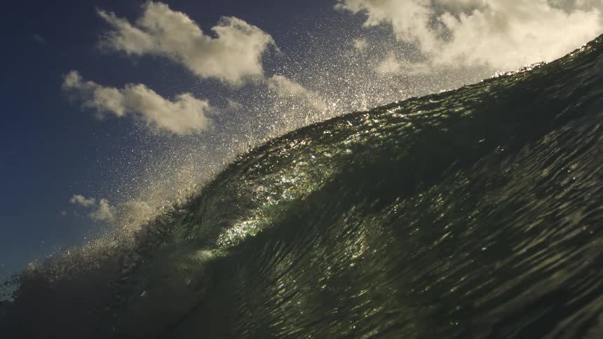 A breathtaking slow-motion shot from within an ocean wave as it crests and barrels, with the sun backlighting the sparkling sea spray