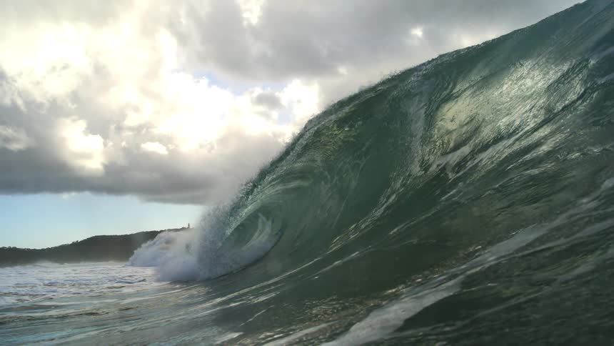 A powerful ocean wave curls and barrels towards the shore in dramatic super slow motion under a cloudy sky
