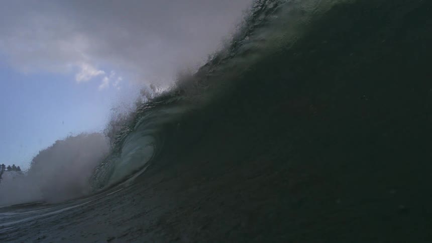 An epic, dark green ocean wave barrels in dramatic super slow motion under a moody, overcast sky