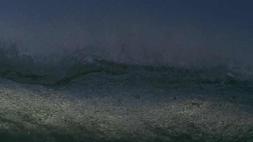 Dramatic slow-motion shot from the water's surface as a powerful ocean wave crashes over the camera against a blue sky