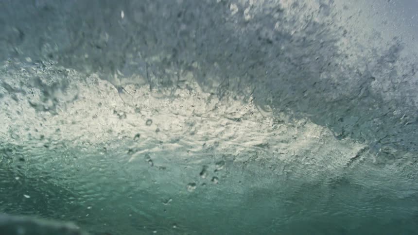 Extreme slow motion view from the water's surface as a powerful ocean wave crests and crashes, pulling the viewer underwater into a sea of bubbles