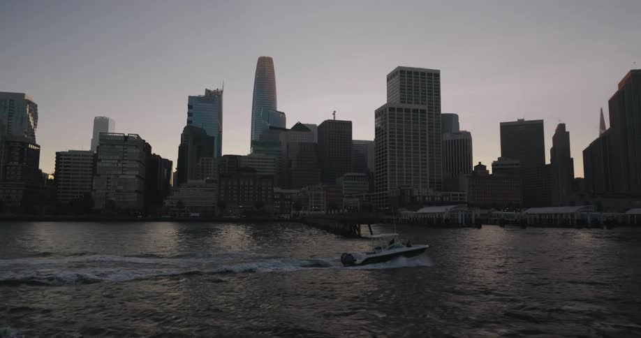A sleek motorboat glides across the water in slow motion with the San Francisco city skyline in the background at sunset