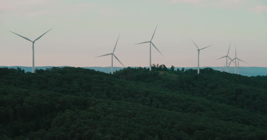A row of wind turbines spins slowly on a lush green mountain ridge at dusk