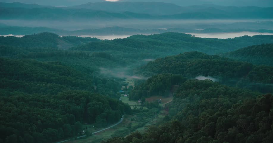 A tranquil, static shot captures misty fog settling in a lush green mountain valley at dawn