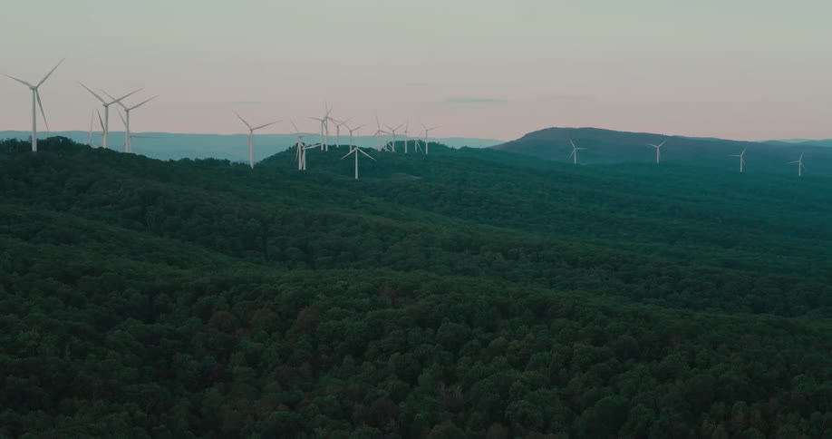 A sprawling wind farm generates clean energy as turbines spin atop rolling, green hills at twilight