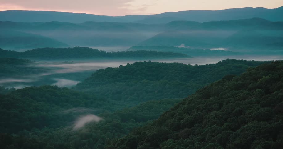 A tranquil and misty view of a rolling green mountain range with fog filling the valleys at twilight